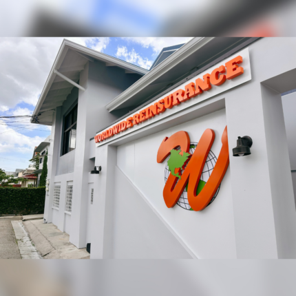 Exterior building signage featuring bold raised lettering spelling “Worldwide Reinsurance” along with a large branded logo mounted on a modern white facade under a partly cloudy sky.