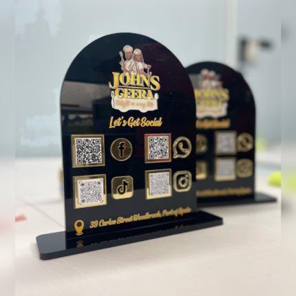 Black acrylic countertop display sign featuring a business logo, multiple QR codes, and social media icons including Facebook, Instagram, TikTok, and WhatsApp, designed for easy customer engagement and contact access.