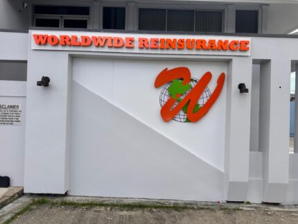 Exterior building sign for Worldwide Reinsurance featuring bold orange 3D lettering and a globe logo with a stylized “W” mounted on a white wall